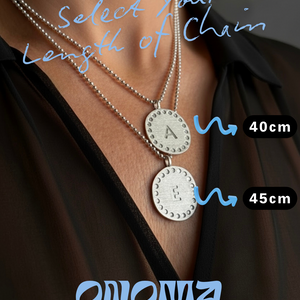Two silver necklaces with two circular initial pendants labeled 'A' and 'E', displayed on a person wearing a dark outfit.
